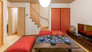 Ein modernes Wohnzimmer mit einer Holztreppe, einem Esstisch gedeckt mit blauem und weißem Geschirr sowie einem Fernseher auf einer Holzkommode.