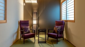 Ein traditioneller japanischer Raum mit Tatami-Böden, zwei violetten Stühlen mit floralen Kissen, einem kleinen Tisch und einem verschiebbaren Shoji-Bildschirm.