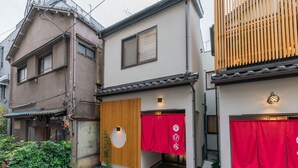 Ein traditionelles japanisches Haus mit Holzhauseingang, rotem Vorhang und einem kleinen Garten mit Topfpflanzen.