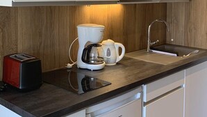 Une cuisine moderne avec des meubles blancs, un four à micro-ondes encastré, une machine à café et un grille-pain.