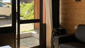 Une pièce dotée d’une porte-fenêtre coulissante donnant sur un espace extérieur, d’un canapé en cuir noir et d’une table blanche.