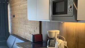 Une cuisine moderne équipée d’un four à micro-ondes encastré, d’une machine à café et d’un grille-pain. Un mur d’accent en bois et un coin salon avec un banc complètent l’ensemble.