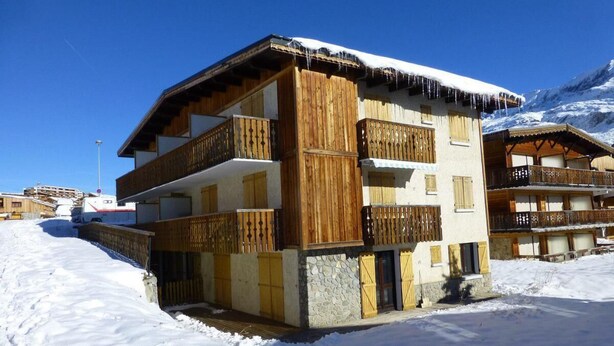 A multi-story chalet with wooden balconies, set in a snowy landscape with mountains in the background. - 2nd floor, tv, ski locker, 25m², Alpe d'Huez (L'Alpe d'Huez)