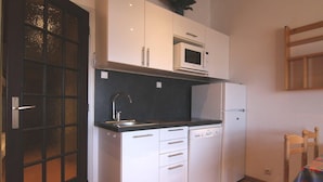 Una cocina compacta con armarios blancos, microondas, lavavajillas y refrigerador.