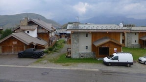 Una hilera de casas de madera tradicionales con cimientos de piedra, una camioneta blanca estacionada al frente y un paisaje montañoso de fondo.
