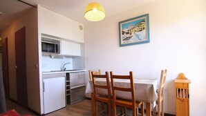A compact kitchen with a microwave, stove, and sink. There is a dining table with chairs and a small cabinet. A painting hangs on the wall, and a wooden cabinet is beside the table. - 150m from ski slopes, 2nd floor, tv, ski locker, 22m², Alpe d'Huez (L'Alpe d'Huez)