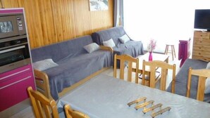Una habitación acogedora con techo de madera, un sofá, una mesa de comedor y un televisor.