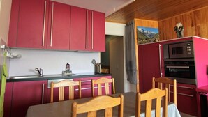 Cocina compacta con gabinetes rojos, techo de madera y una zona de comedor con mesa y sillas.
