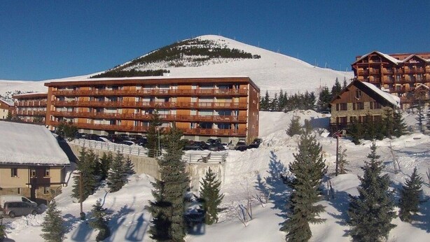 Un edificio de madera de varios pisos con balcones, rodeado de terreno y árboles cubiertos de nieve.