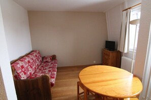 A room with a wooden floor, a round wooden table, a red and white patterned sofa, and a television on a wooden cabinet. - 220m from ski slopes, 3rd floor, tv, ski locker, 22m², Alpe d'Huez (L'Alpe d'Huez)