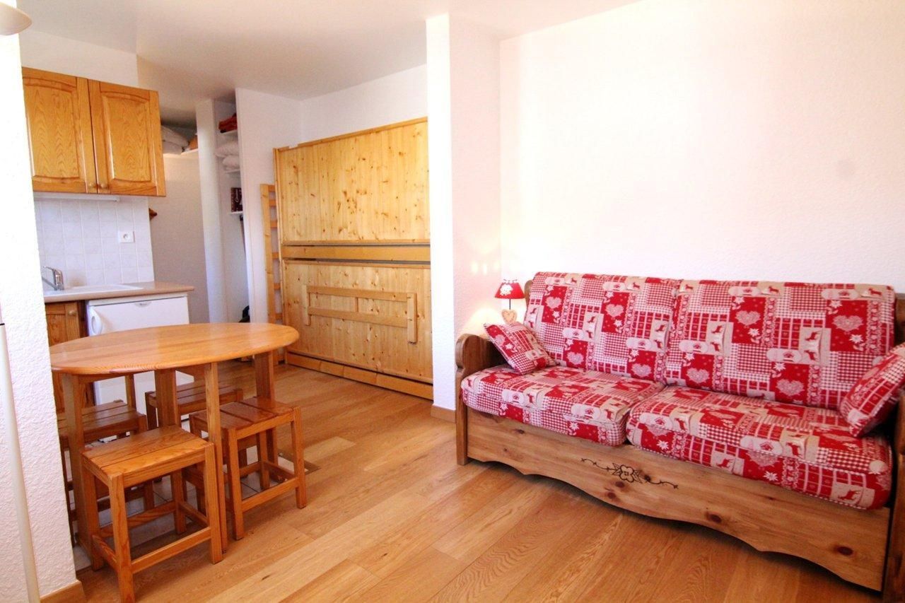 Ein gemütlicher Wohnraum mit Küchenzeile, einem Holzespeisetisch mit Stühlen und einer Couch mit rot-weißer Musterdecke.