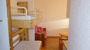 Habitación pequeña con una litera, una mesita y una silla.