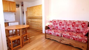 Un espacio habitable pequeño con una mesa y sillas de madera, un sofá con funda a cuadros rojos y blancos, y armarios de madera.