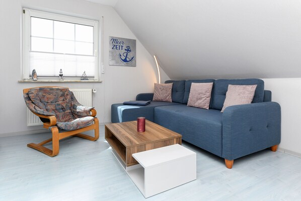 A modern living room with a blue sofa, a wooden coffee table, and a patterned armchair.