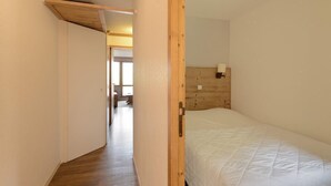 Ein schmaler Flur führt zu einem Schlafzimmer mit einem hölzernen Bettrahmen und einer weißen Bettdecke.