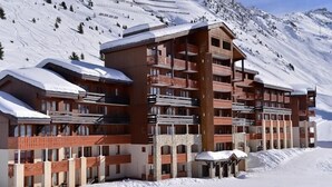Ein mehrstöckiges Hotel mit Balkonen vor einer verschneiten Bergkulisse.