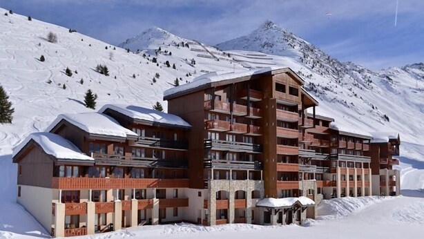 Ein mehrstöckiges Hotel mit Balkonen vor einer verschneiten Bergkulisse.