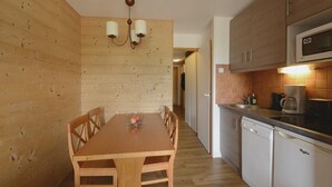Ein Essbereich mit Holzwandverkleidung, einem Holztisch und -stühlen, einer Chandelieber sowie eine Küche mit Mikrowelle und Geschirrspüler.