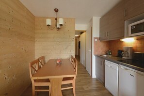 Un comedor con paneles de madera, una mesa y sillas de madera, una araña y una cocina con microondas y lavavajillas.