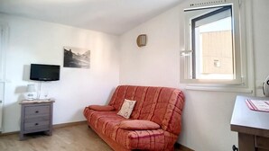 Ett litet, möblerat rum med en soffa, en tv, ett litet bord och ett fönster med utsikt.