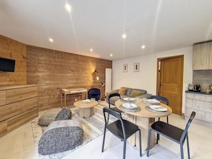 A modern living room with a wooden wall, a dining table set for four, and a kitchen area with a toaster. - 200m from resort center, Ground floor, balcony, tv, ski locker, 47m², Saint Martin de Belleville (Saint-Martin-de-Belleville)
