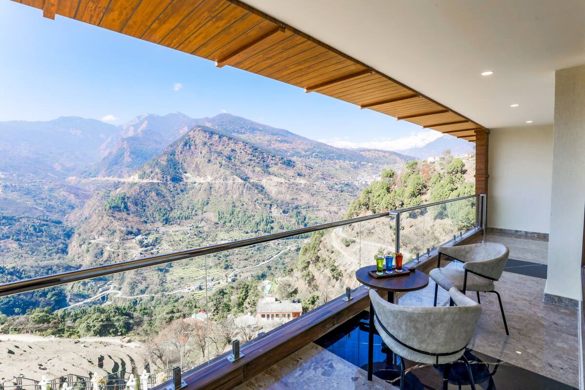 Ein Balkon mit Blick auf eine Berglandschaft, einem Tisch mit Stühlen und einem Glasgeländer.