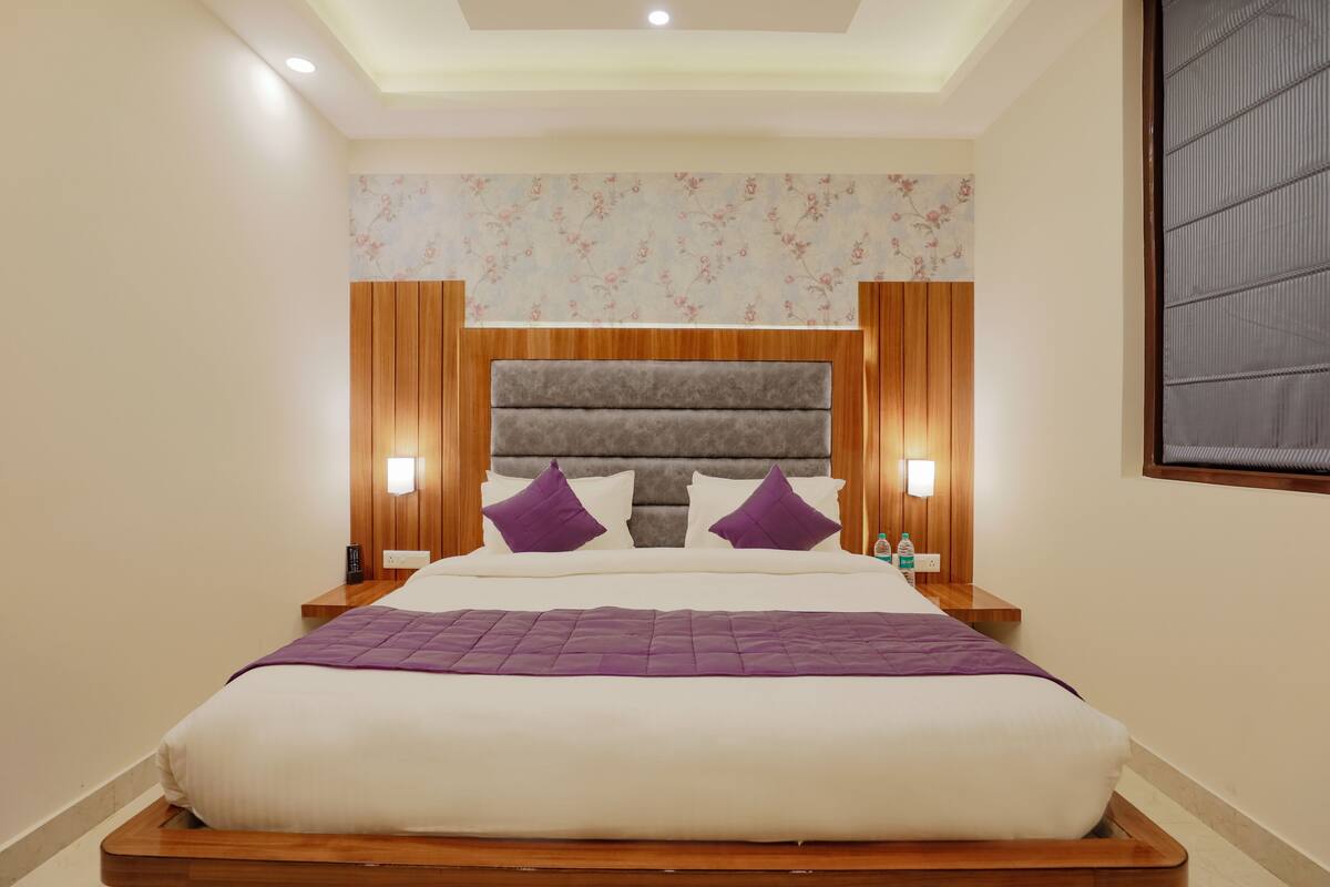Ein ordentlich bezogenes Bett mit hölzernem Kopfteil, zwei Nachttischlampen und einer Wand mit Blumenmuster.