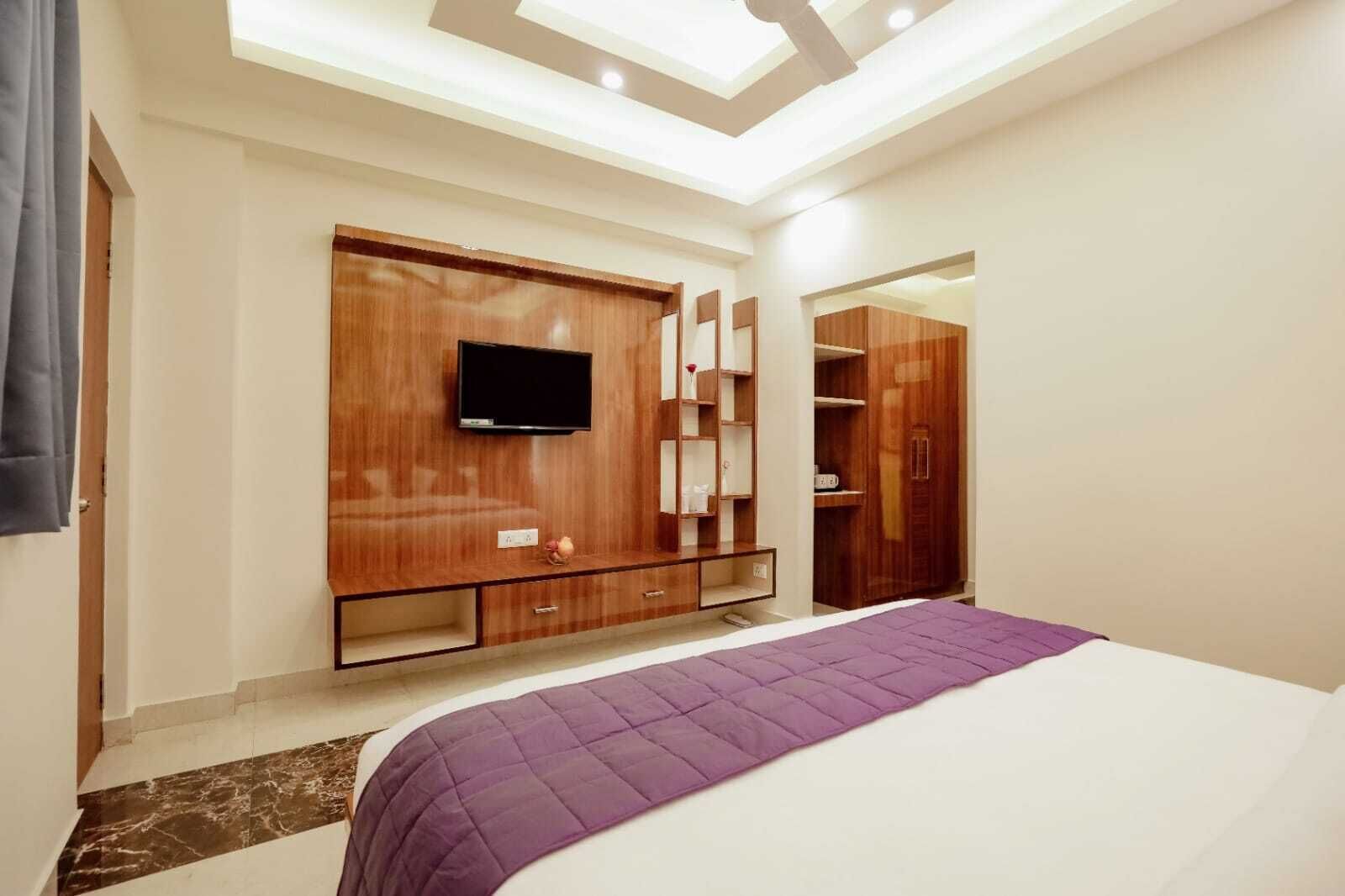 A bedroom with a bed, a TV mounted on a wooden cabinet, a wardrobe, and a mirror.