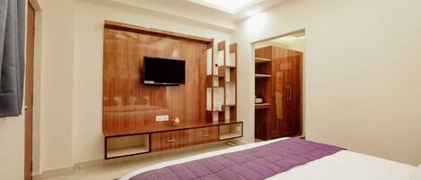 A bedroom with a bed, a TV mounted on a wooden cabinet, a wardrobe, and a mirror.