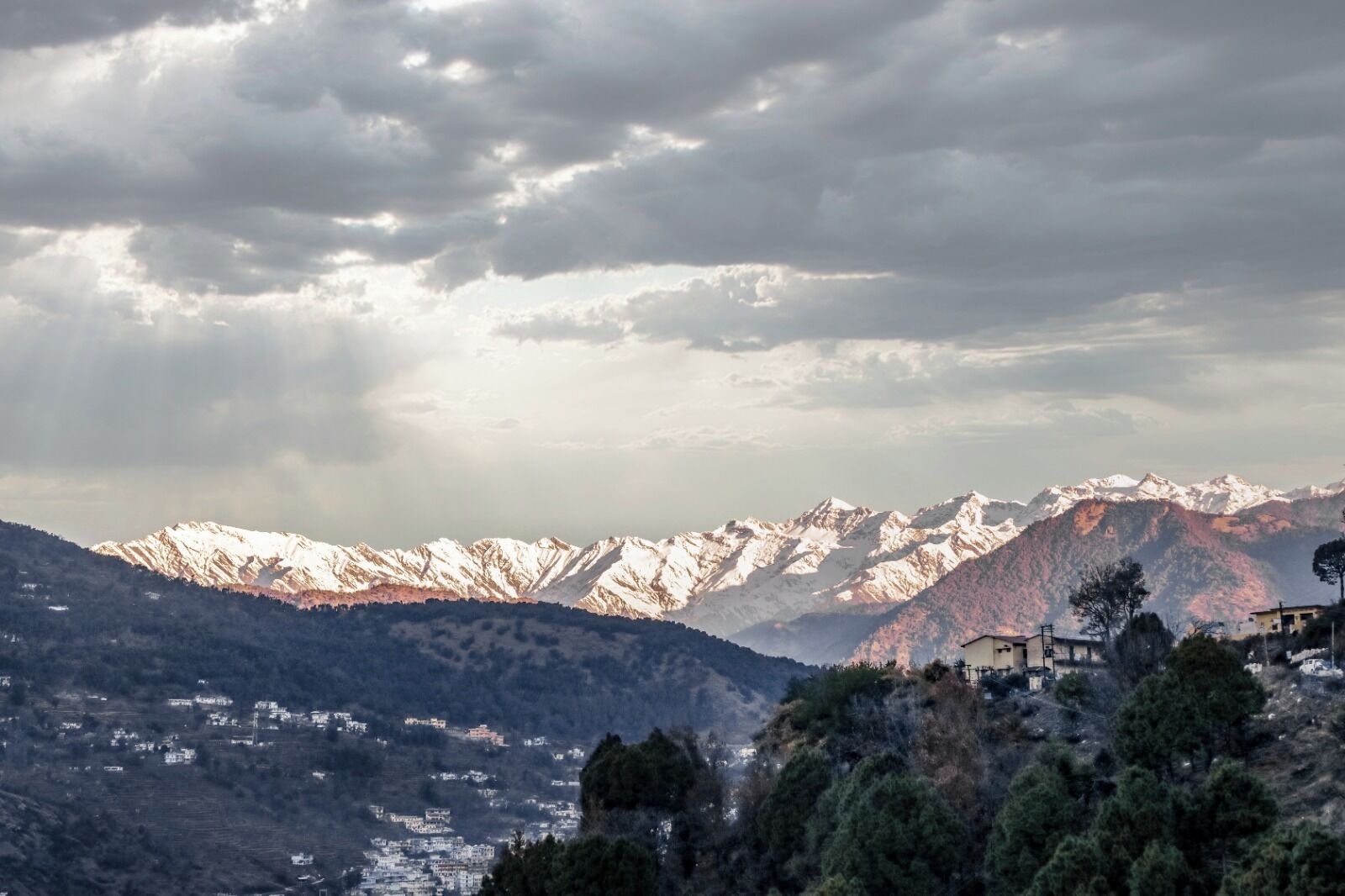 Un paisaje montañoso con picos nevados, un valle con edificios dispersos y un cielo nublado.