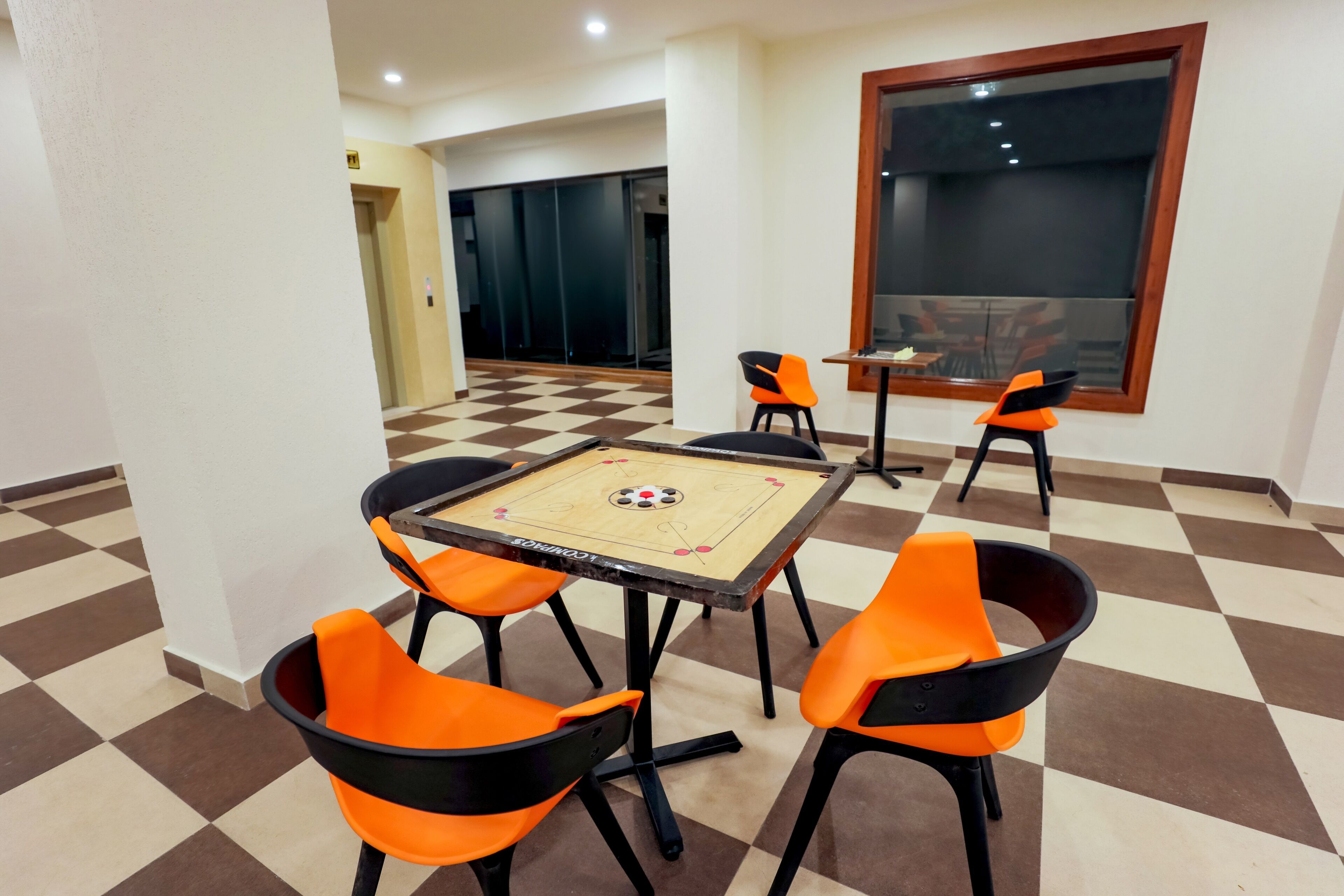 Een kamer met een zwart-wit geruite vloer, een tafelvoetbaltafel en oranje stoelen.