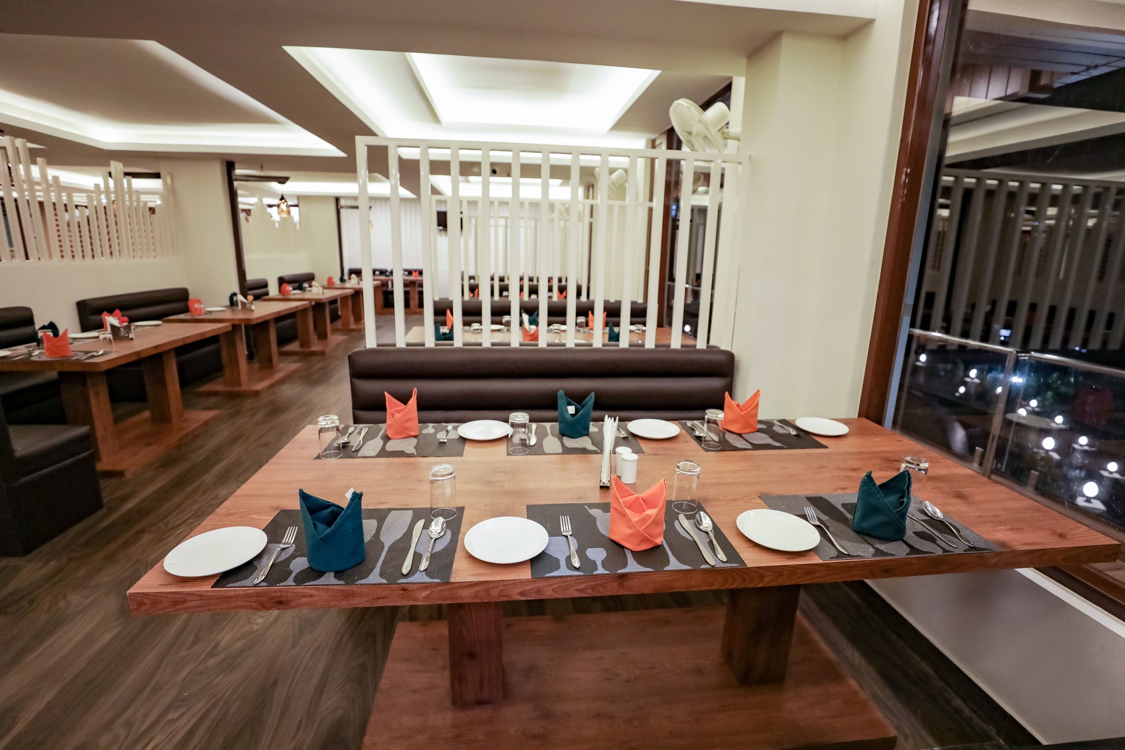 A restaurant with wooden tables, black placemats, and orange napkins.
