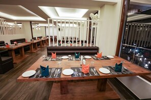 A restaurant with wooden tables, black placemats, and orange napkins. - Regenta Resort Madhuganga Ukhimath (Ukhimath)