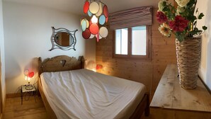 Una habitación de madera con una cama, un espejo colgado en la pared, una lámpara colgante y una ventana con cortinas.