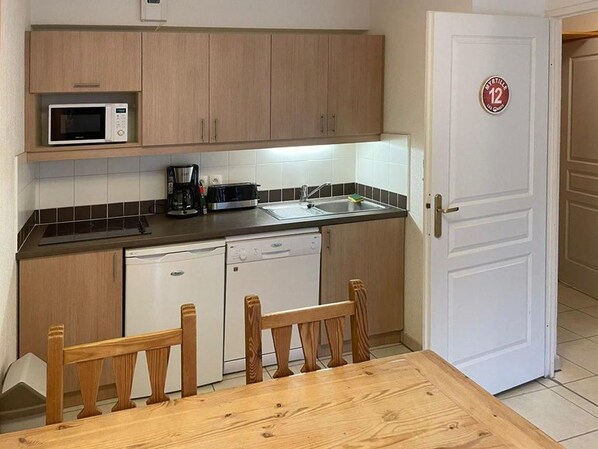 Cocina compacta con armarios de madera, microondas, cafetera y lavavajillas.