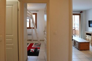 Un pasillo con una escalera, una puerta que da a una habitación con televisión y un ventanal con cortinas.