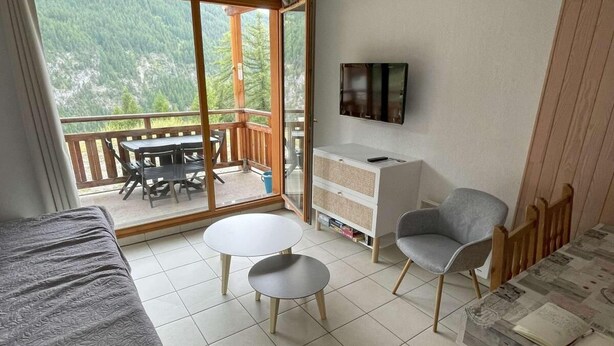 Una habitación con cama, dos mesitas, sofá, televisor y balcón con mesa y sillas.