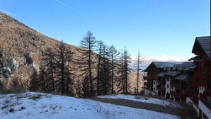 Un paisaje nevado con una hilera de edificios de madera, probablemente un albergue de montaña, con vistas despejadas del bosque y las montañas circundantes.