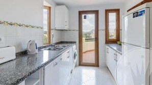 A compact kitchen with white cabinets, a granite countertop, a washing machine, and a refrigerator. - La Manga Club El Rancho Townhouse 399 (La Manga Club, Cartagena)