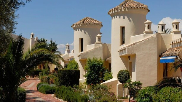 A pathway leading to a row of buildings with a dome and bell towers, surrounded by greenery. - La Manga Club El Rancho Townhouse 399 (La Manga Club, Cartagena)