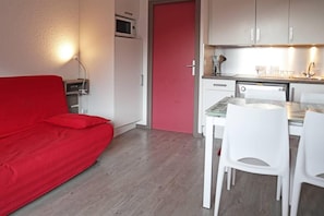 A compact living space with a kitchenette, a dining area with white chairs, and a red sofa.