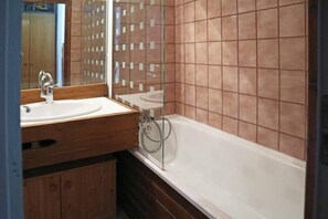 A bathroom with a wooden vanity, a white sink, a mirror, and a bathtub with brown tiles.