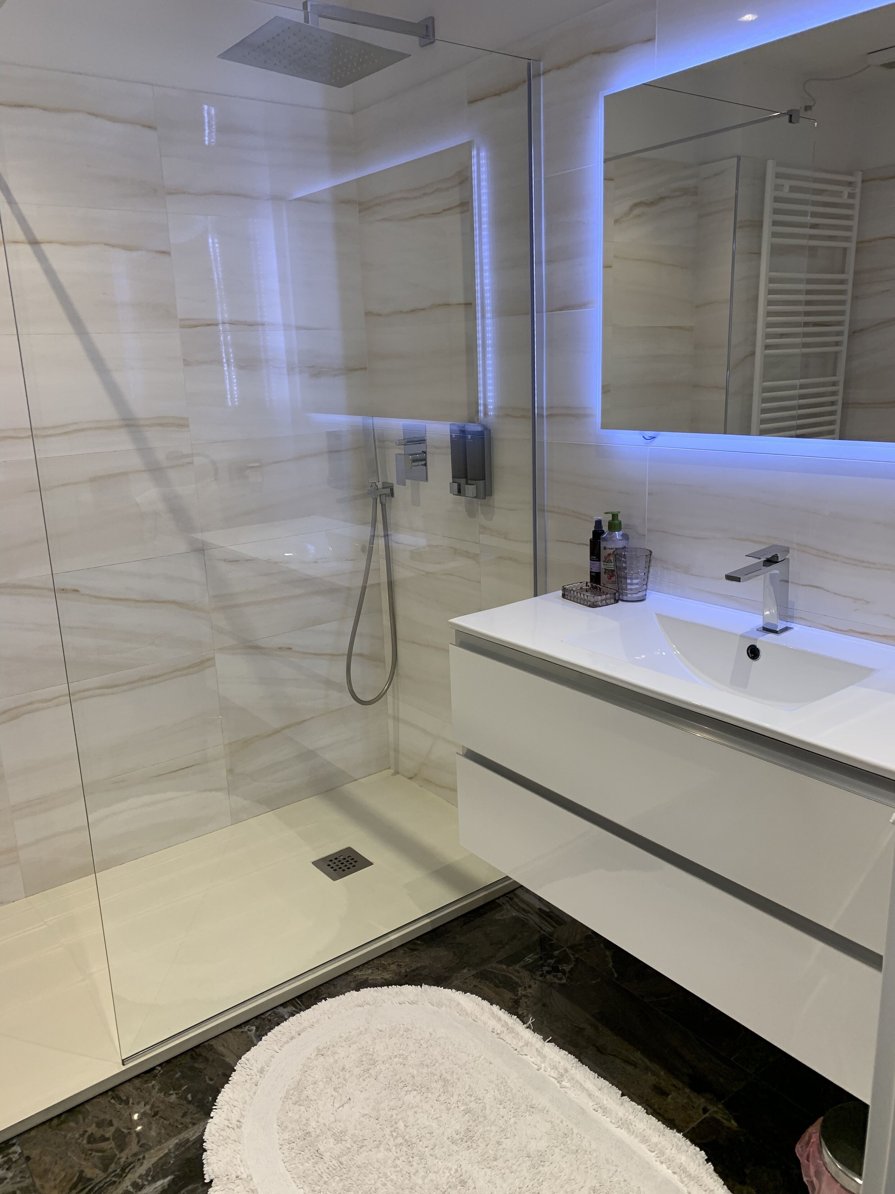 Uma casa de banho moderna com chuveiro em cabine de vidro, toucador branco com lavatório e um espelho grande.