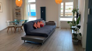 A modern living room with a sofa, dining table, and chairs. There are two hanging lights, a radiator, and a window with a view. - Center Salo’, near to Duomo,  to Vittoriale D’Annunzio (Salò)