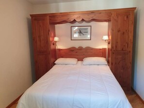 A bedroom with a wooden headboard, two bedside lamps, and a framed picture on the wall.