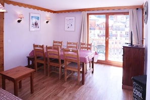 A dining area with a table set for four, wooden chairs, a bench, and a view of buildings through a glass door. - Ski-in/ski-out & foot of the slopes, 2nd floor, view ski slopes, swimming pool, sauna, balcony, tv (Les Orres)