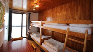 Une chambre avec des lits superposés, des murs en bois et un plancher en bois. Il y a une fenêtre donnant sur l’extérieur.