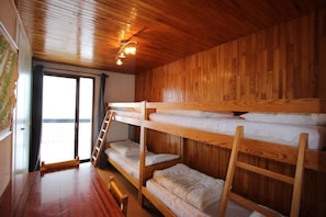 Een slaapkamer met stapelbedden, houten wanden en een houten vloer. Er is een raam met uitzicht.