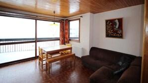 Un salon avec un plafond en bois, un canapé marron, une table à manger avec des chaises et une grande fenêtre donnant sur un beau paysage.