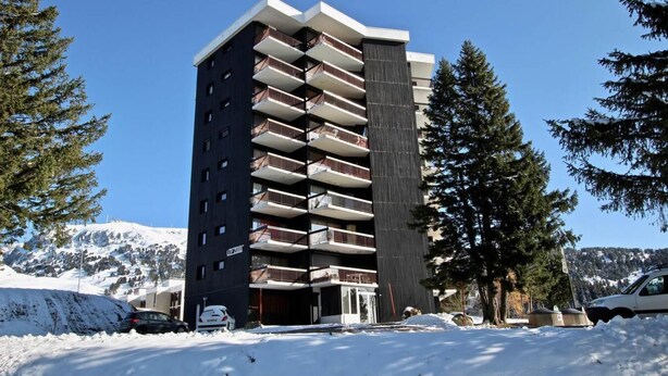 Un hôtel à plusieurs étages, doté de balcons, entouré d’un paysage enneigé et d’arbres.